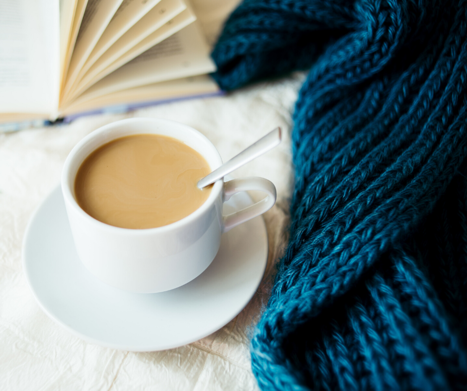 a cup of tea beside a knitted blue scarf and a book